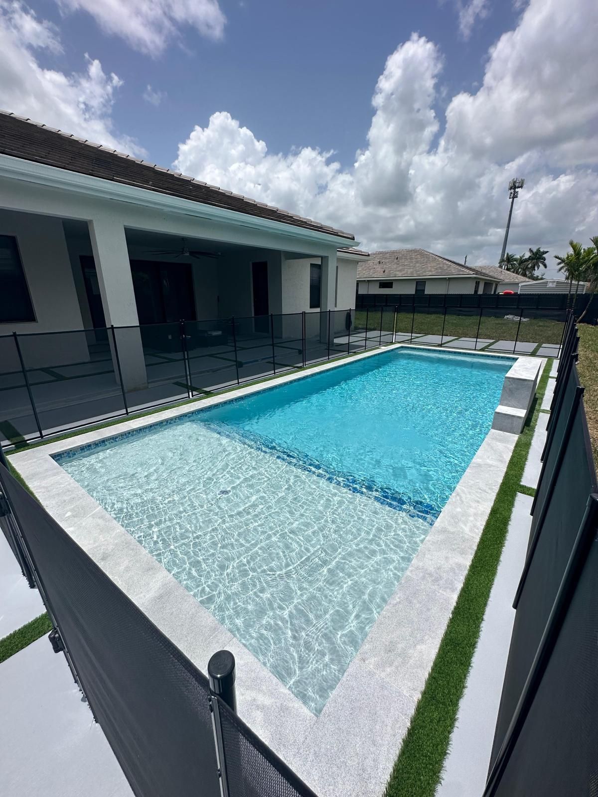 A large swimming pool is in the backyard of a house.