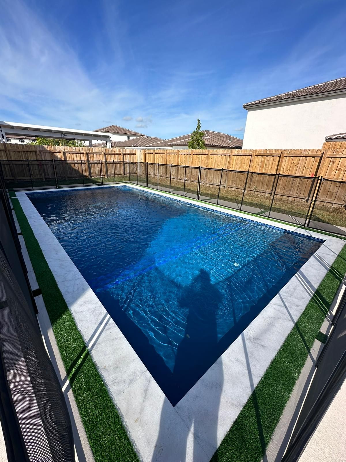 A large swimming pool surrounded by a fence and grass in a backyard.