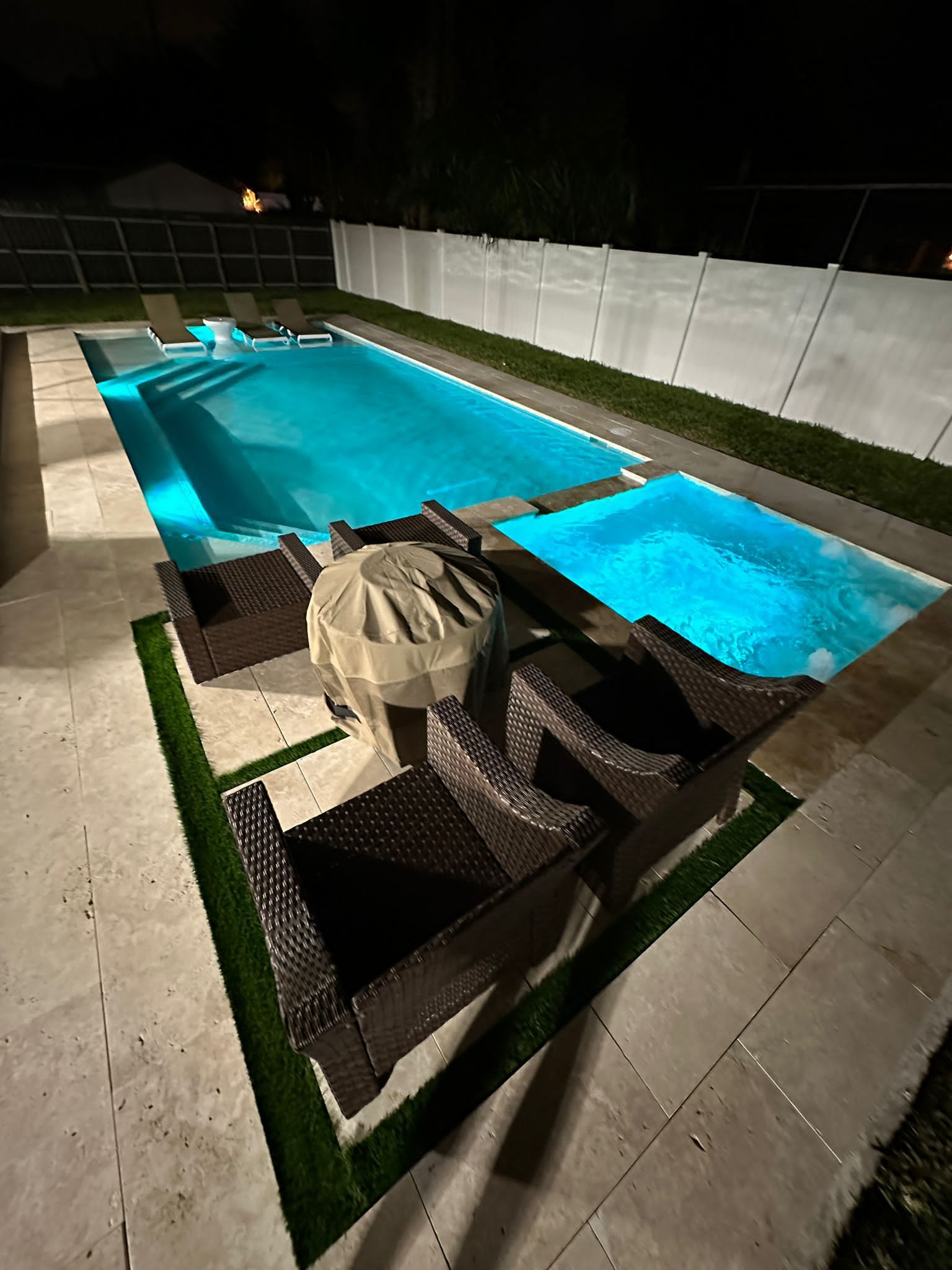 A large swimming pool with a table and chairs around it at night.