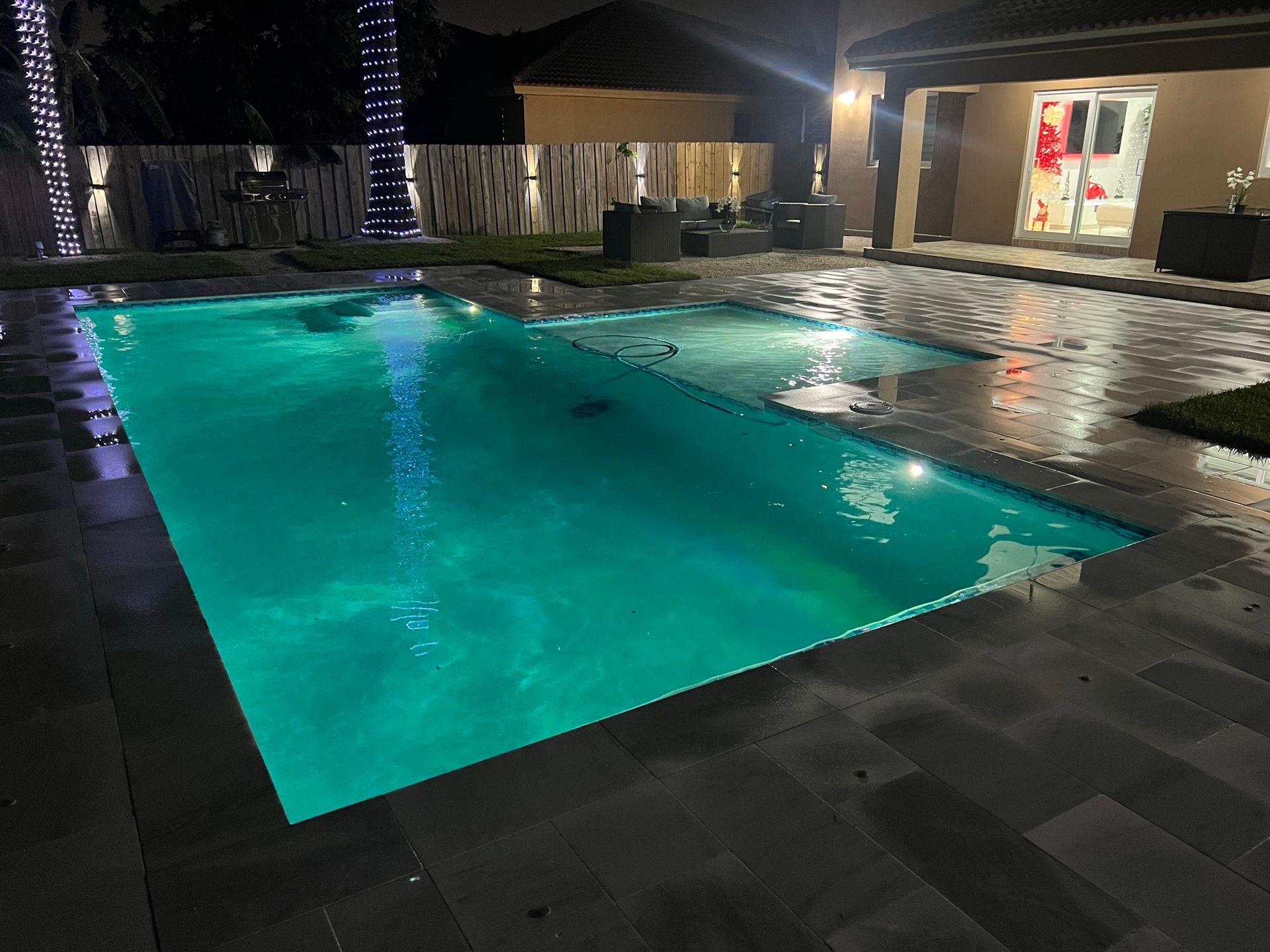 A large swimming pool is lit up at night in front of a house.