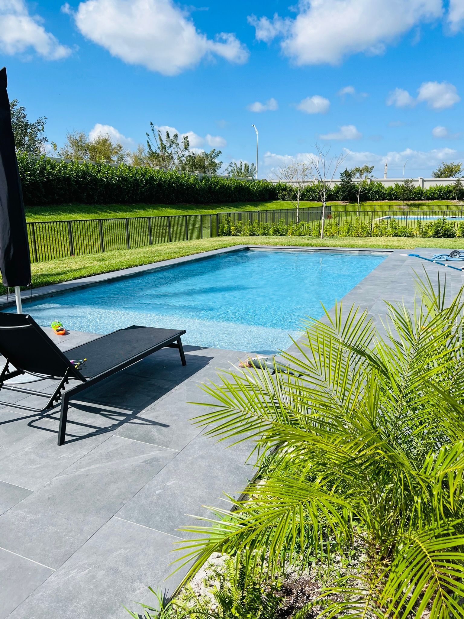 A large swimming pool with a black umbrella and chairs