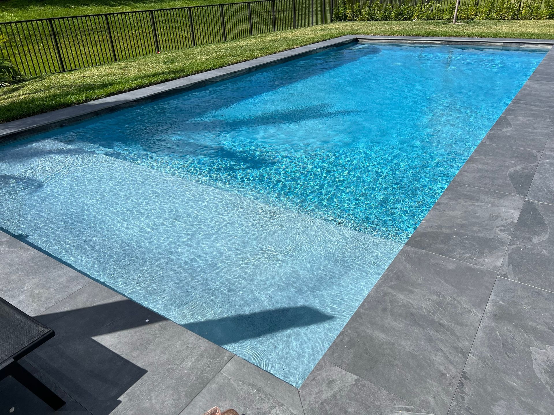 A person 's feet are standing next to a large swimming pool.