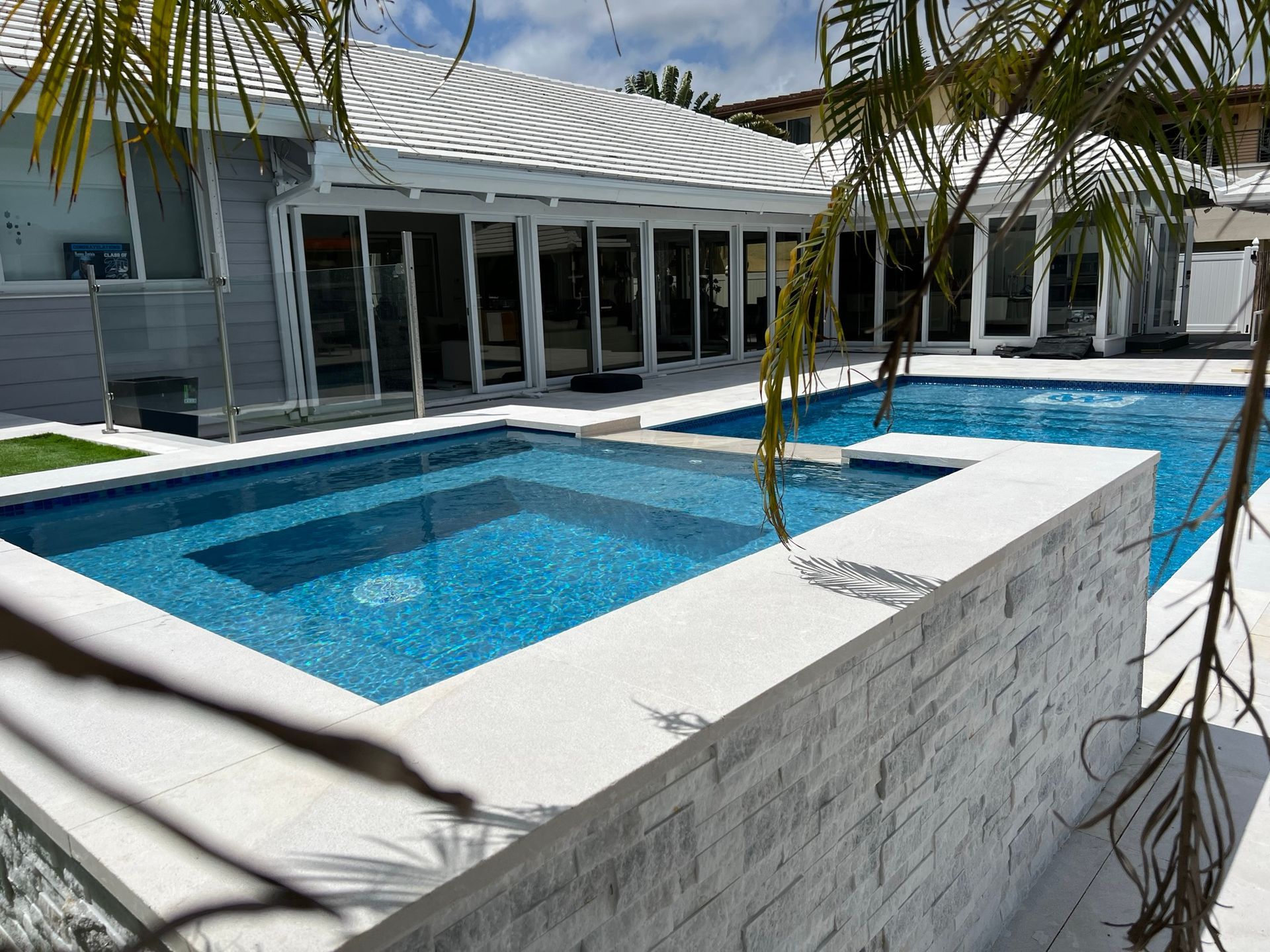 A large swimming pool with a hot tub in the middle of it in front of a house.