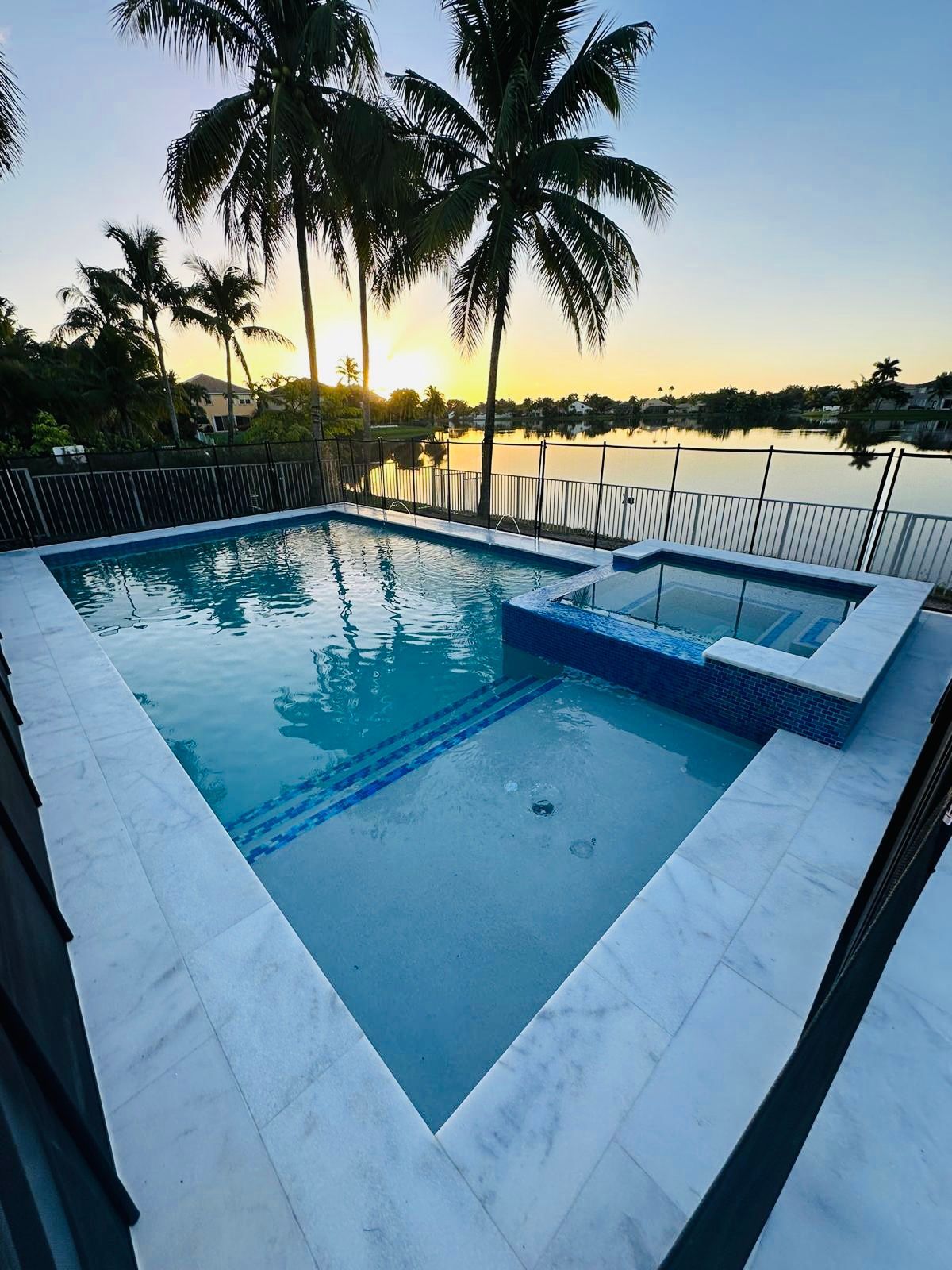 A large swimming pool with a hot tub and palm trees in the background.