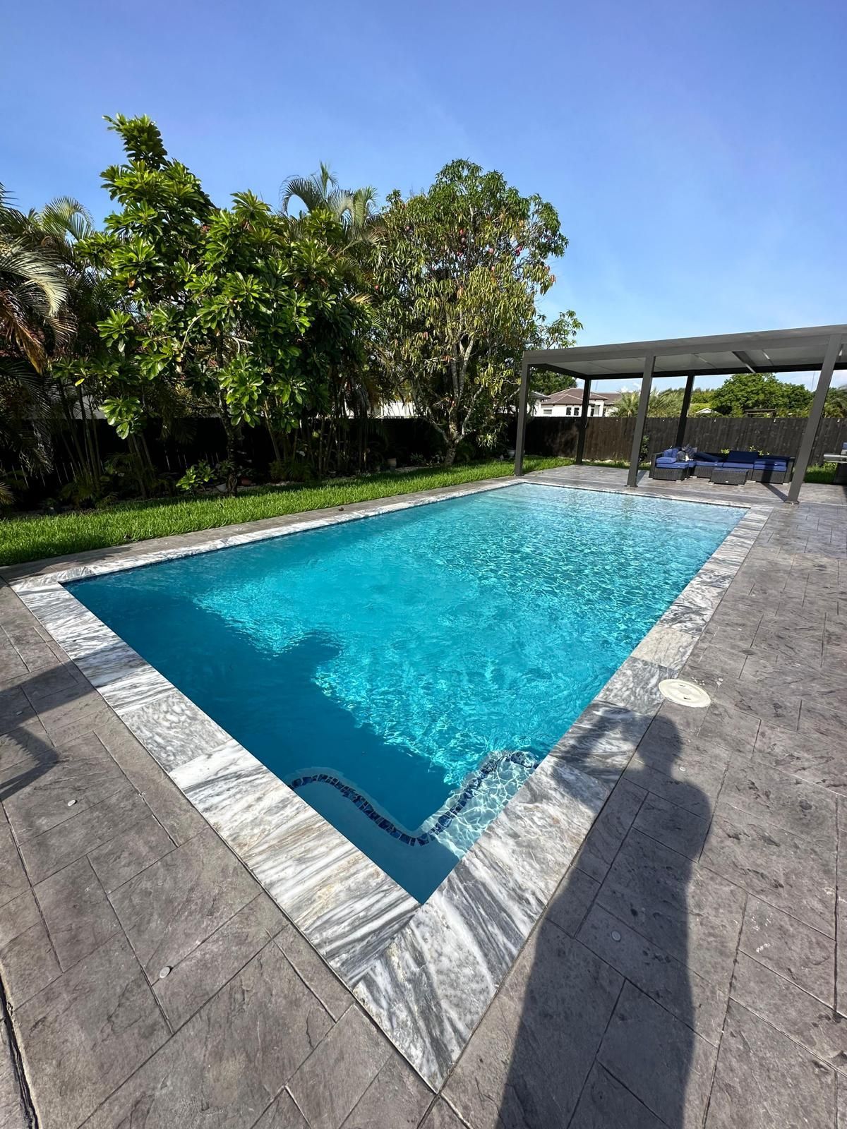 A large swimming pool is surrounded by trees and a pergola