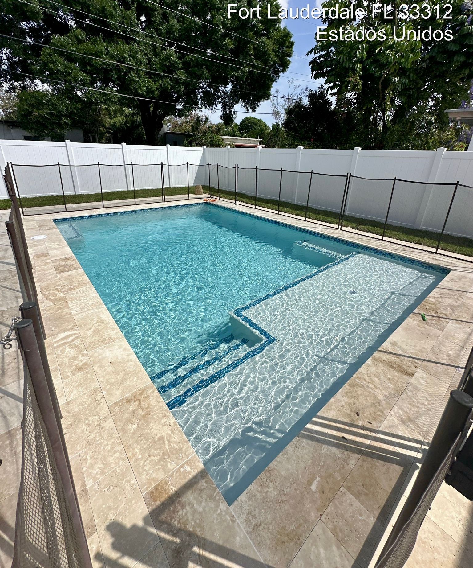 A large swimming pool is surrounded by a fence and trees.