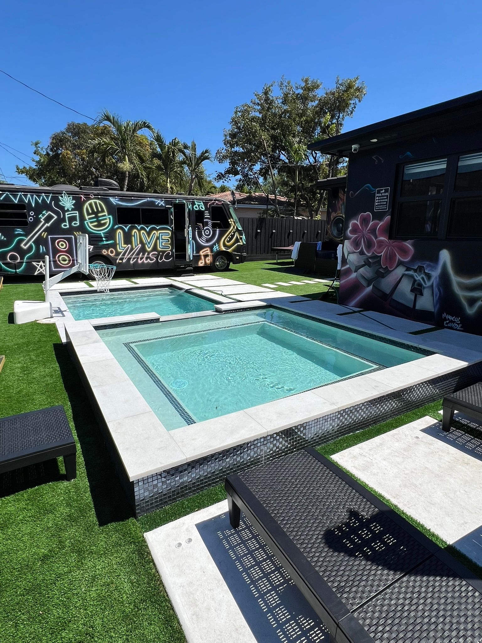 A large swimming pool is surrounded by lawn chairs and a building with graffiti on it.