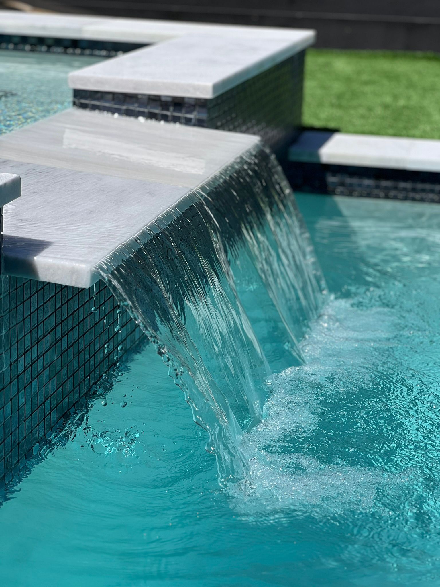 A waterfall is falling into a swimming pool.