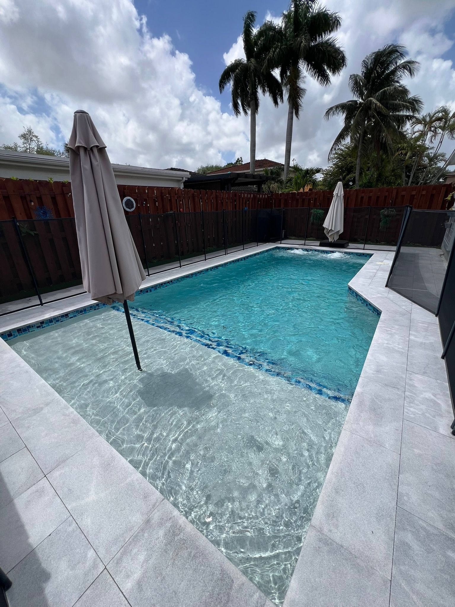 A large swimming pool with umbrellas and palm trees in the background.