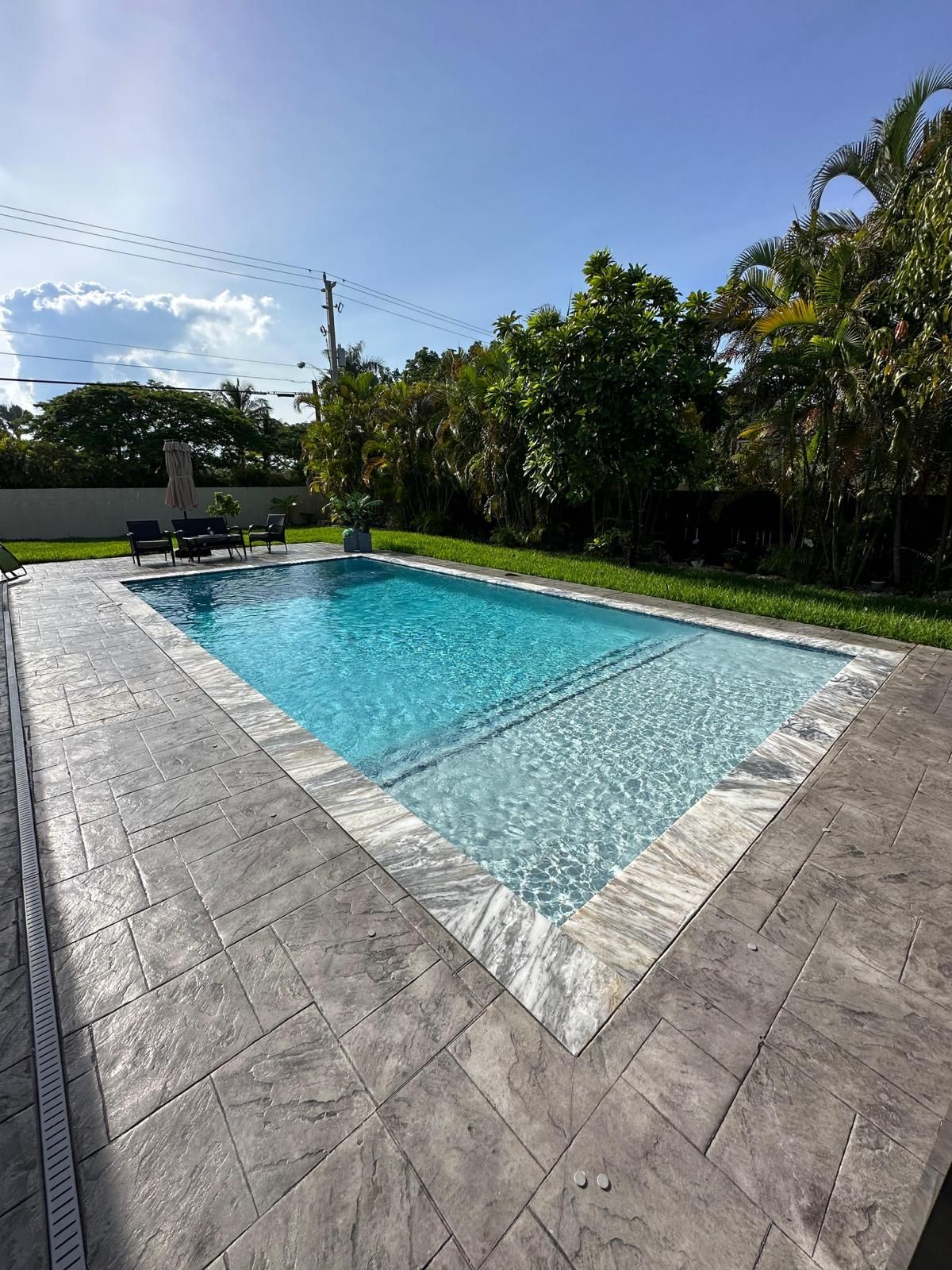 A large swimming pool with a concrete patio in the backyard.