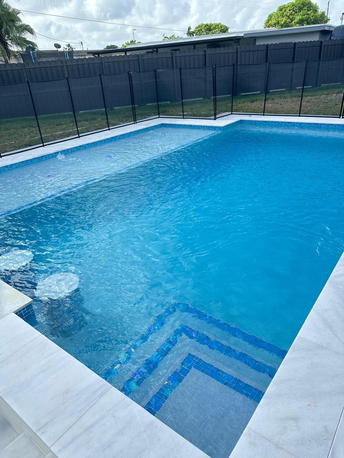 A large swimming pool with stairs and a fence surrounding it.