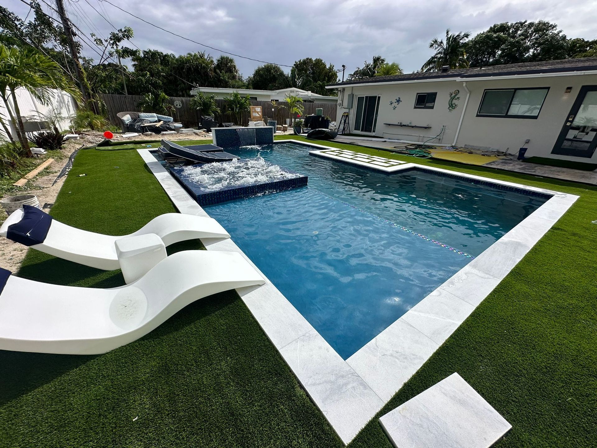 A large swimming pool surrounded by lawn chairs and a house.