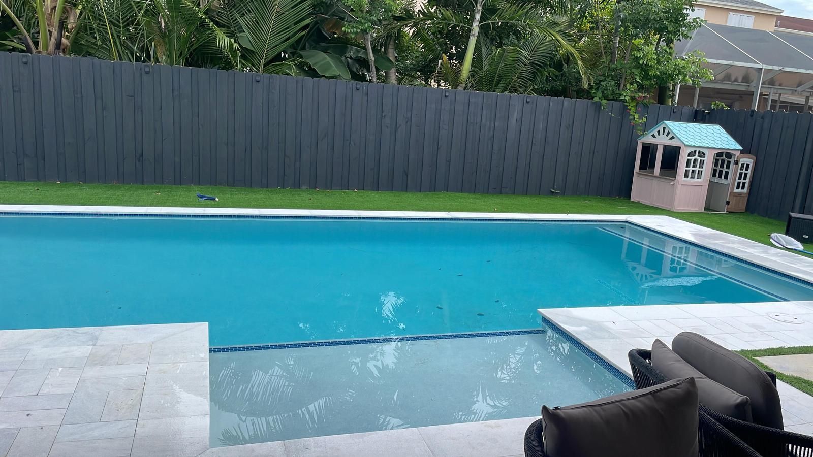 A large swimming pool in a backyard with a fence and a playhouse.