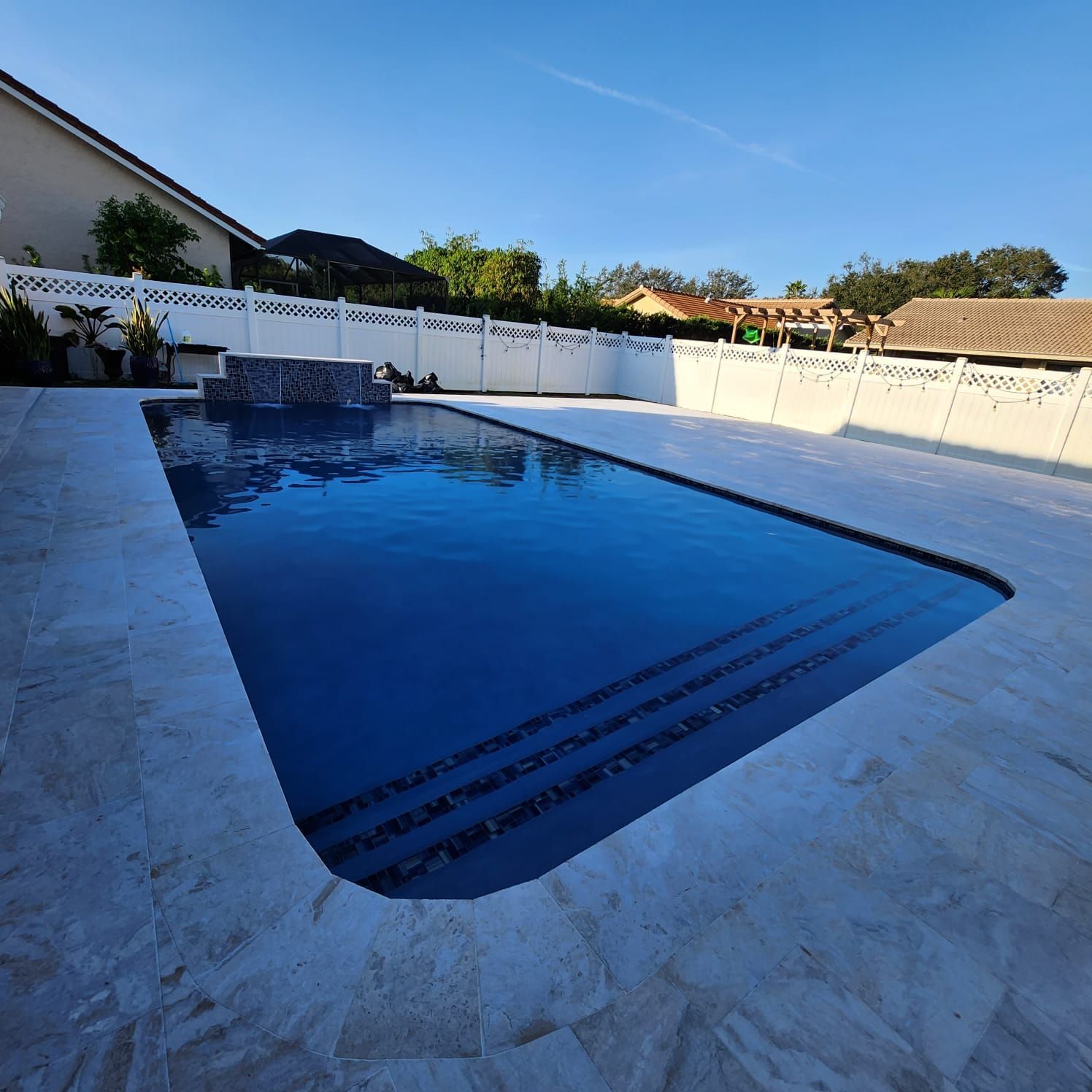 A large swimming pool is surrounded by a white fence
