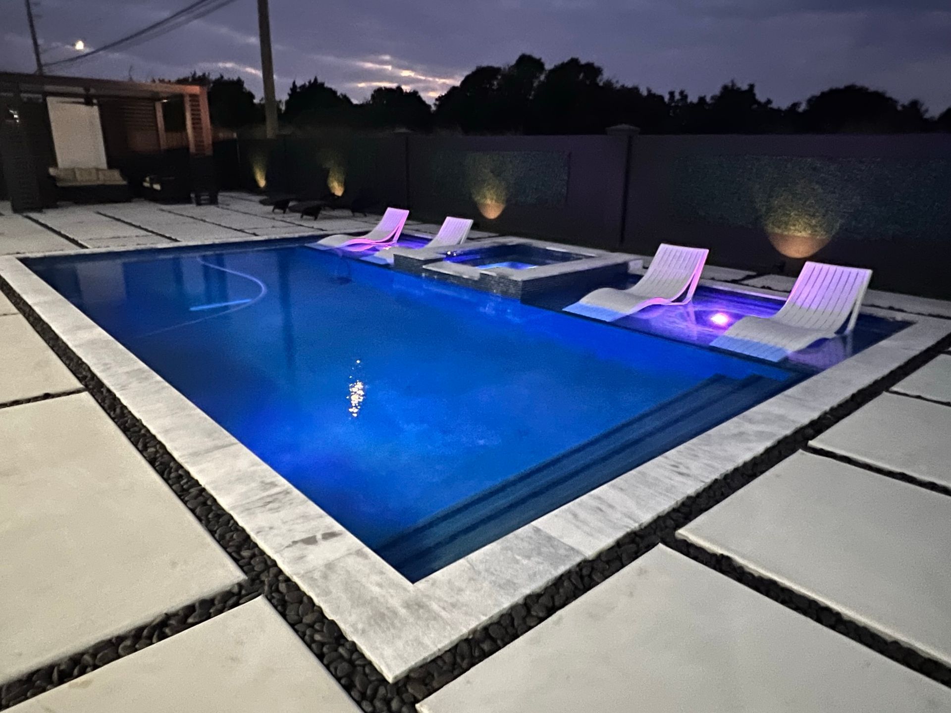 A large swimming pool with chairs around it at night