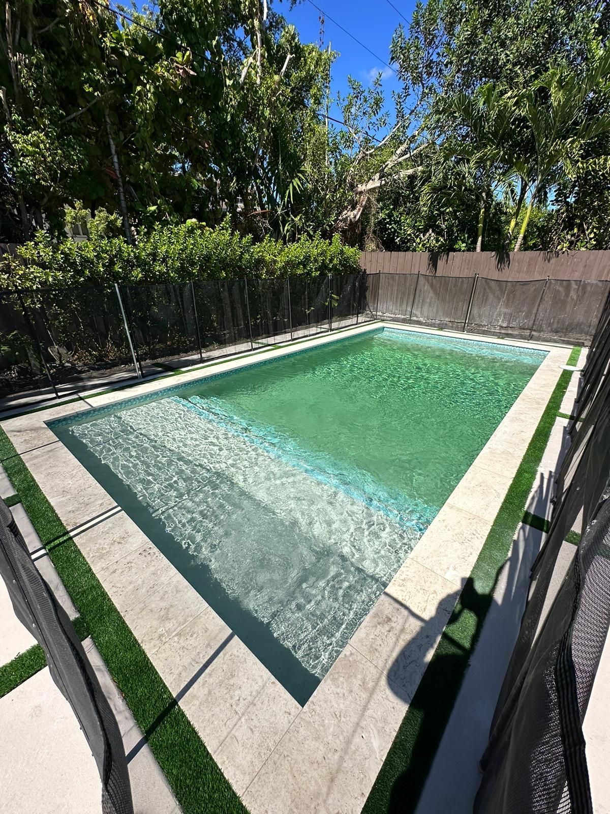 A large swimming pool surrounded by trees and grass in a backyard.