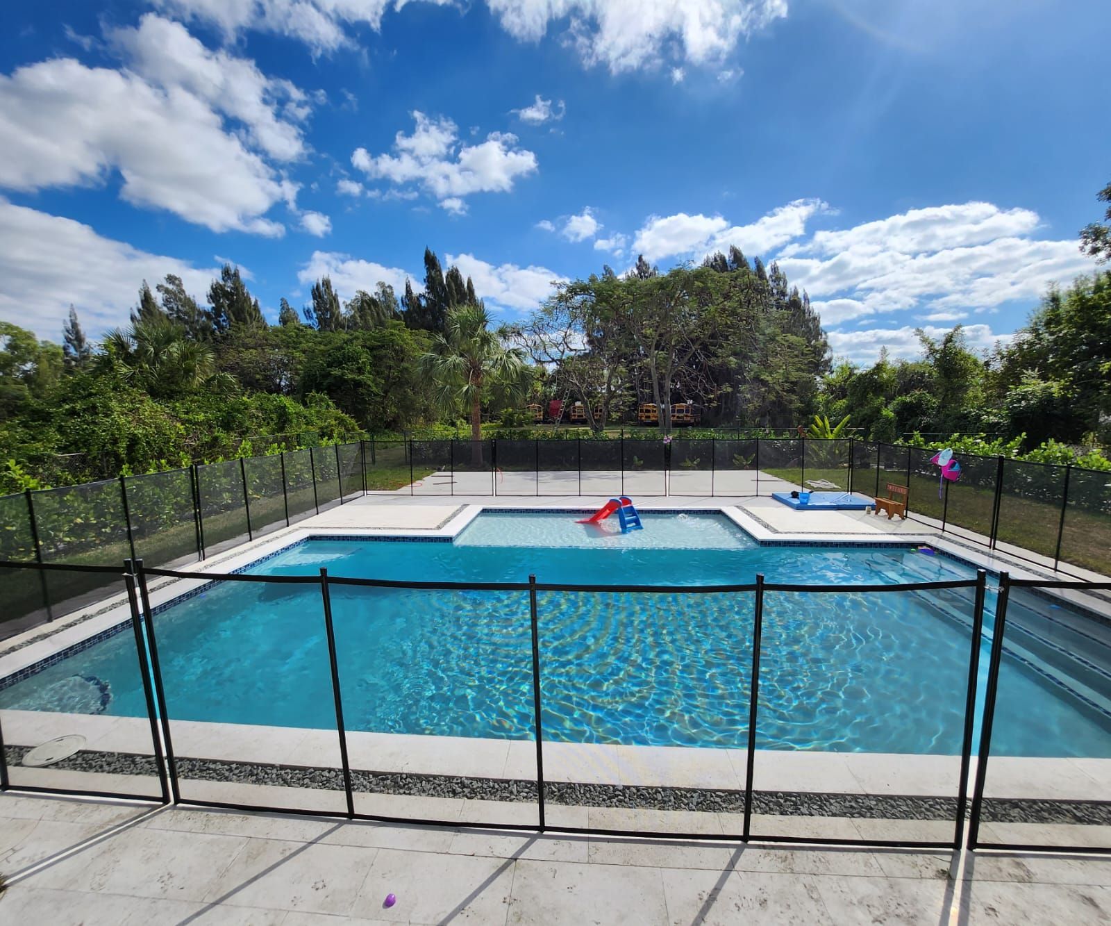 A large swimming pool surrounded by a fence on a sunny day.