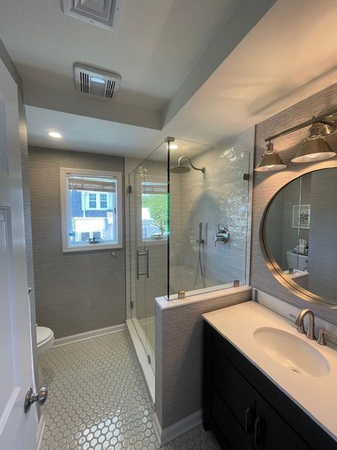 Modern bathroom with glass shower, dark vanity, hex tile floor, and window view outside