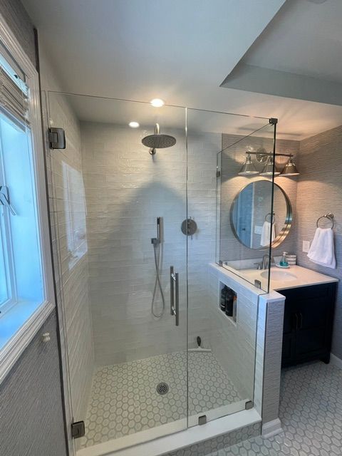 Modern bathroom with glass shower, hex tile floor, and vanity sink with round mirror.