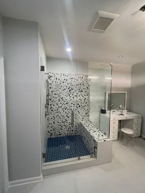 Modern bathroom with glass shower, blue mosaic floor, and white vanity.