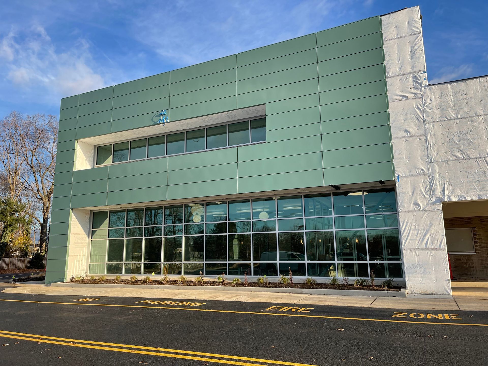 Modern green-and-white building with large glass windows beside a road under a blue sky