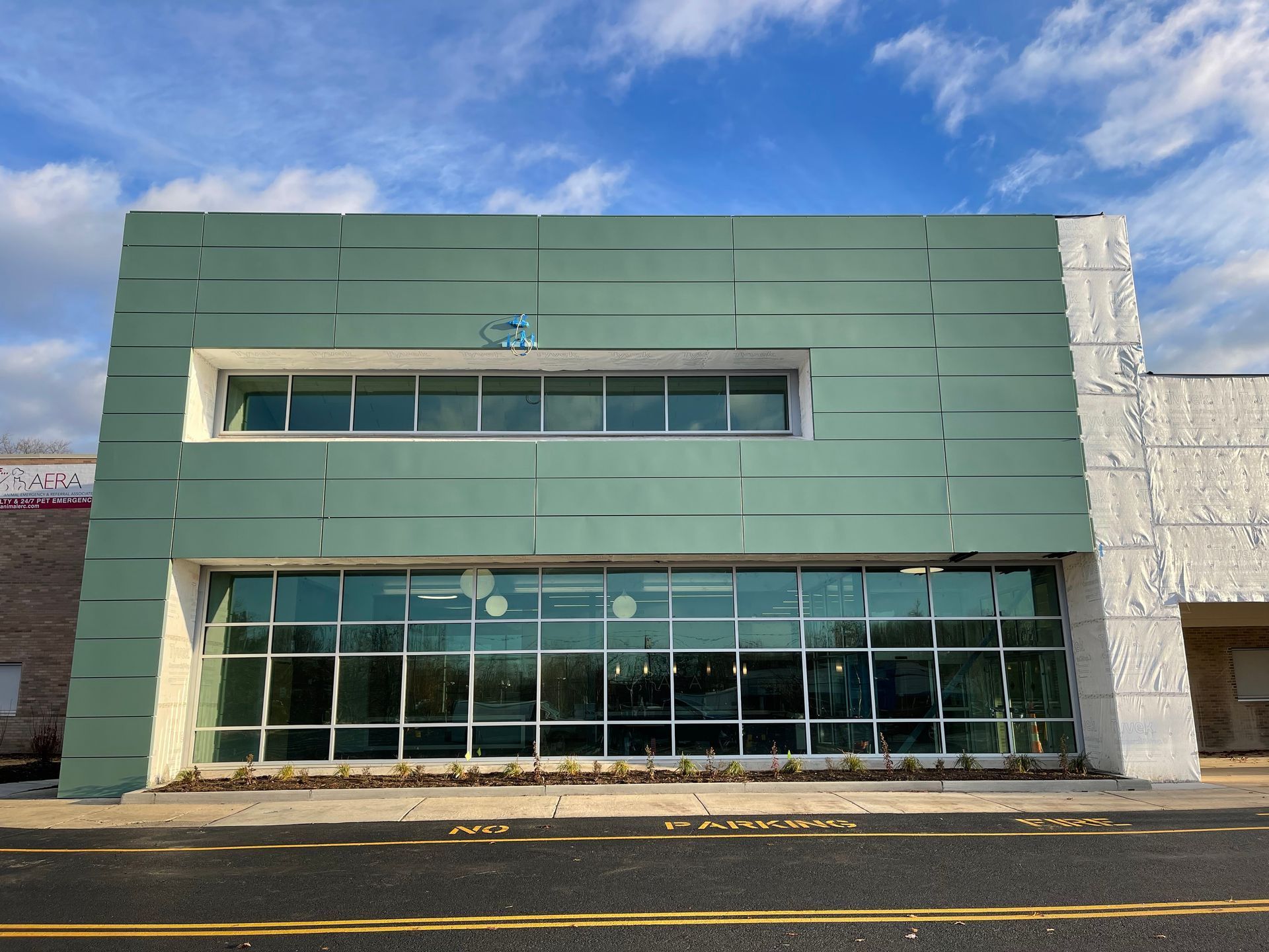 Modern green storefront with large glass windows and a white side wall under a blue sky