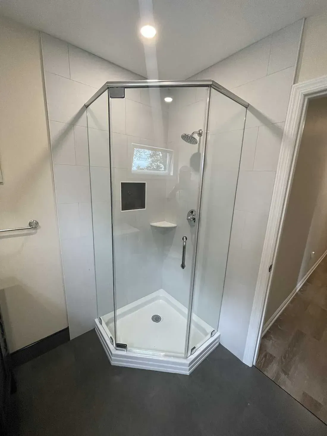 A corner shower with white tiled walls, a glass enclosure, a white base, a small built-in shelf, and chrome fixtures.