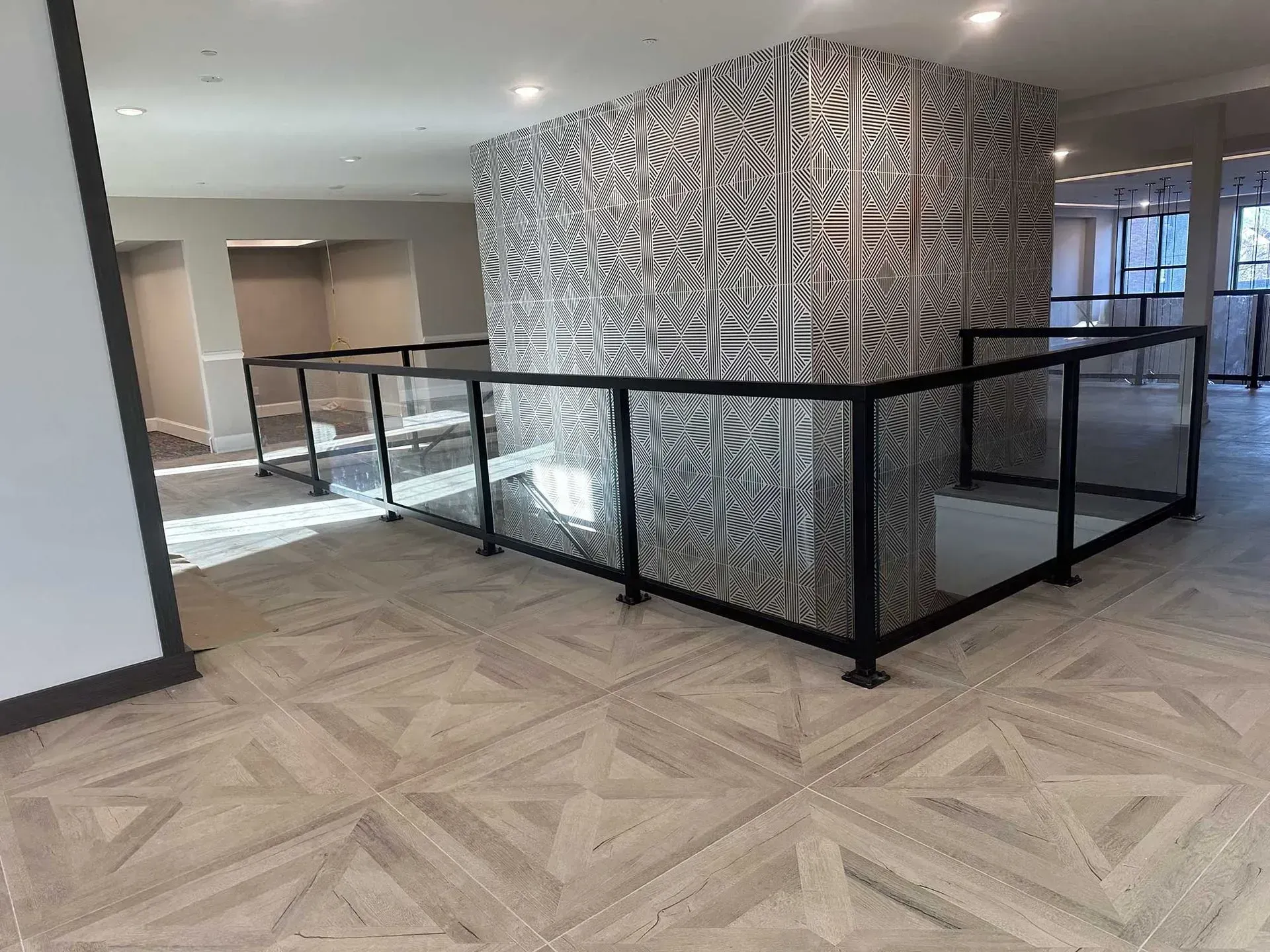 A modern interior with a central column featuring geometric black-and-white tiling, surrounded by black glass railings.