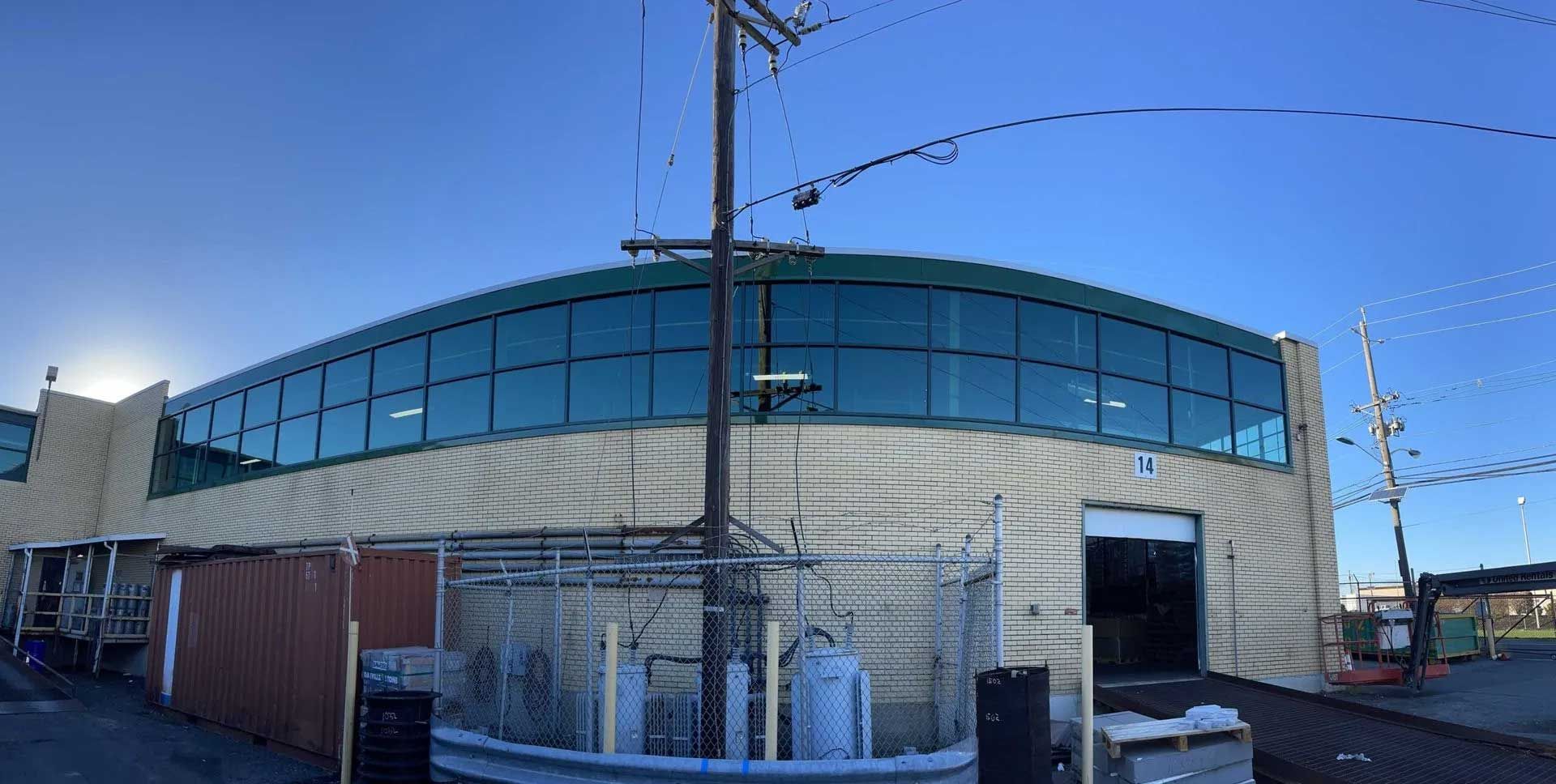 Low-angle view of a beige commercial building with a curved, reflective glass upper level under a clear blue sky.
