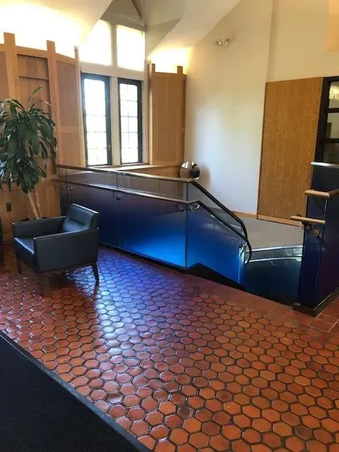 A lobby with hexagonal terracotta floor tiles, a black armchair, and a staircase with a blue glass railing.