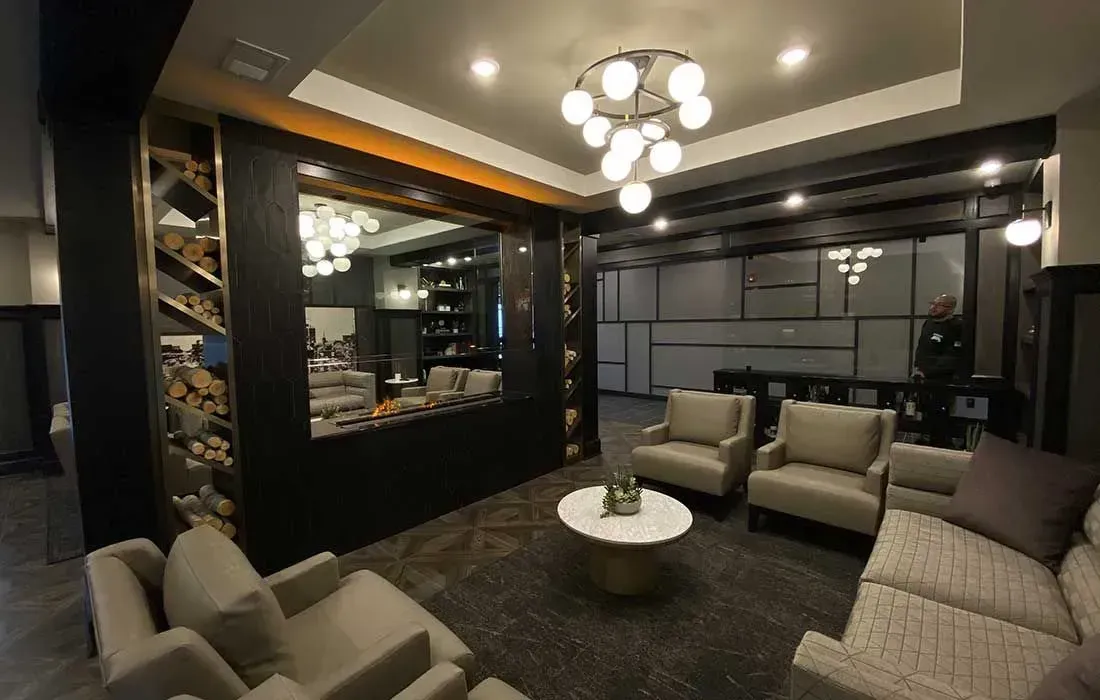 A modern lounge featuring beige armchairs, a patterned sofa, a small white coffee table, and a large central room divider.