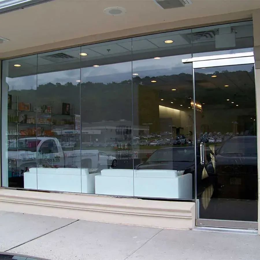 Storefront with large glass windows and a glass door, revealing a bright interior with white seating and shelves of items.