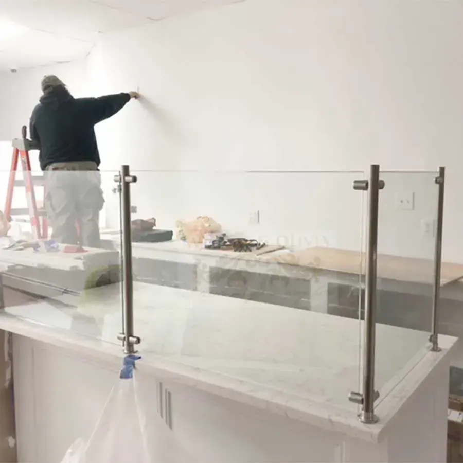 A person on a ladder marks a white wall above a counter with a modern glass and stainless steel railing.