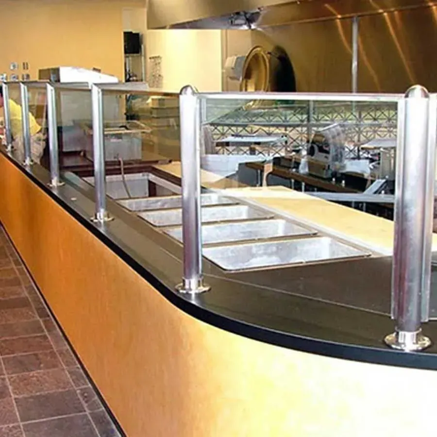 A commercial food service counter with a black top, metal sneeze guards, and a light-colored base in a tiled room.