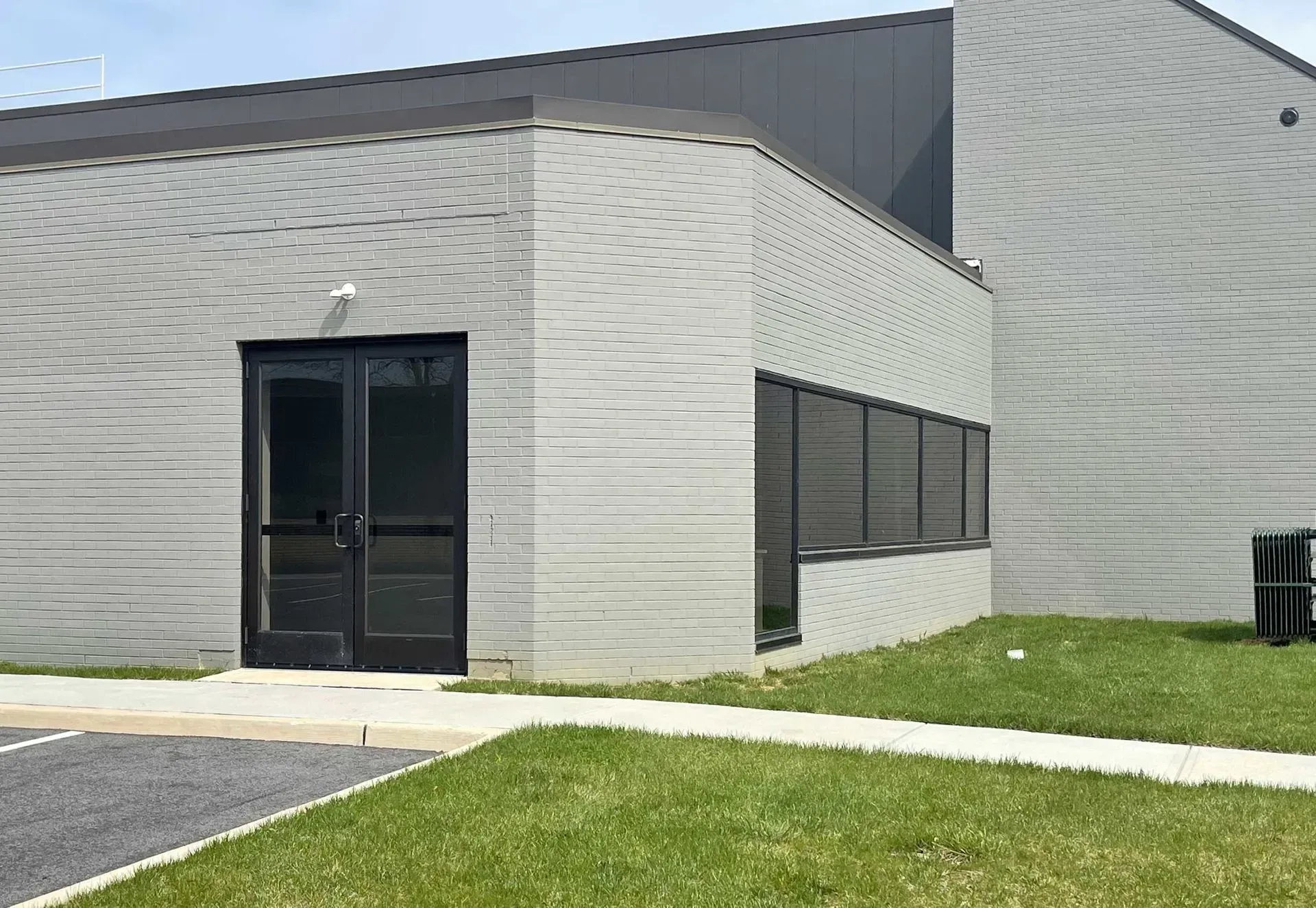 A gray brick commercial building exterior featuring a double-door entrance and a row of windows next to a lawn.