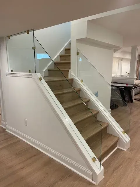 Modern staircase featuring wood treads and glass railings with brass hardware, set within a white-walled interior.