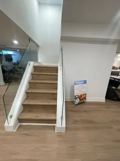 A set of wooden stairs with glass railings in a bright, modern interior room with light-colored walls and flooring.