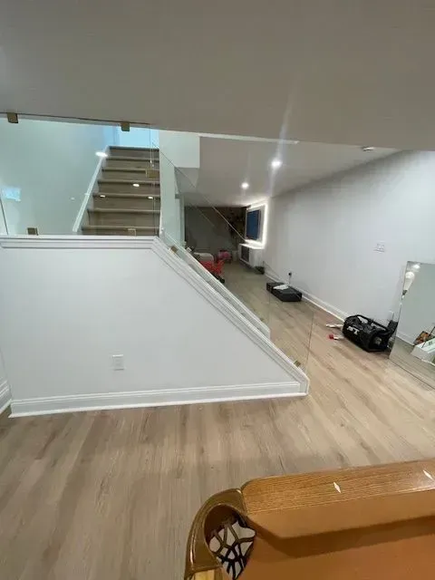 A bright basement with light wood flooring, a white staircase, and a corner of a pool table in the foreground.