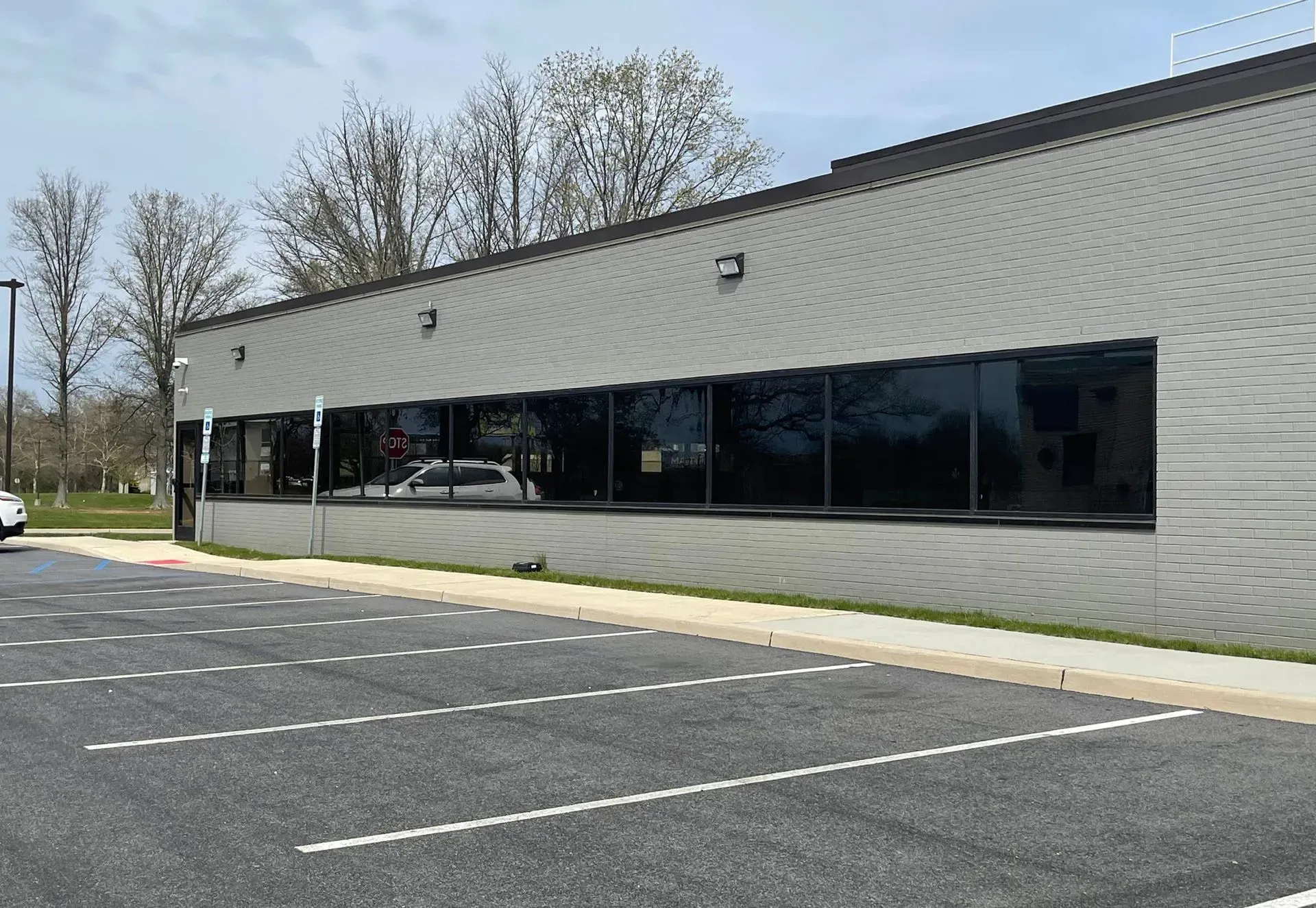 A low, gray, rectangular office building with a long strip of dark tinted windows and a paved parking lot in front.
