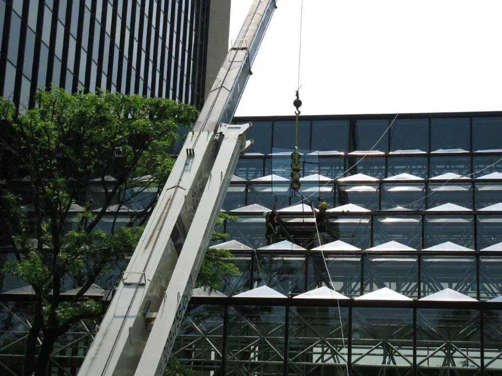 A crane lifts a suspended work platform with two people cleaning the glass exterior of a modern office building.