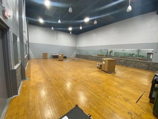 A large, empty hall with hardwood floors, white and gray walls, a black ceiling, and cardboard boxes on the floor.