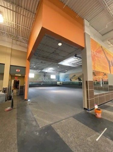 An empty retail space with orange accents, grey flooring, and a mural on the back wall under a high, open ceiling.