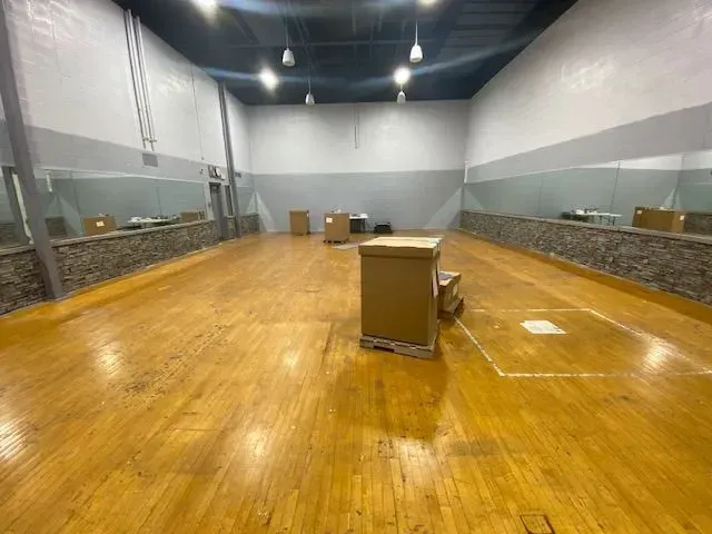 A spacious, empty dance studio with wood flooring, mirrored walls, and several cardboard boxes in the center.