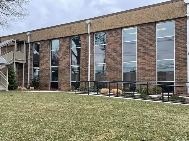 A two-story brick office building with tall, vertical windows and an accessible metal ramp leading to the entrance.