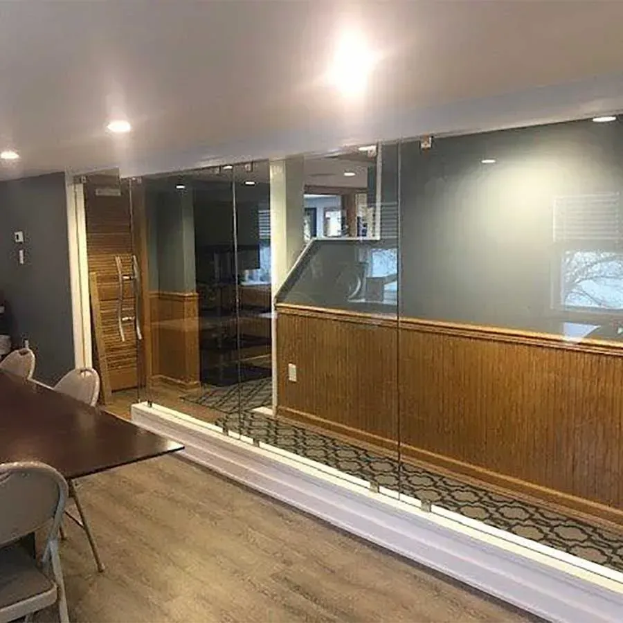 A room with wood-paneled walls and glass partitions, featuring a conference table with chairs on a light wood floor.