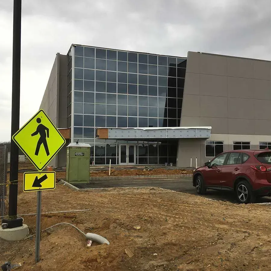 A multi-story building with a large glass facade under construction, with a red SUV, portable toilet, and road sign.