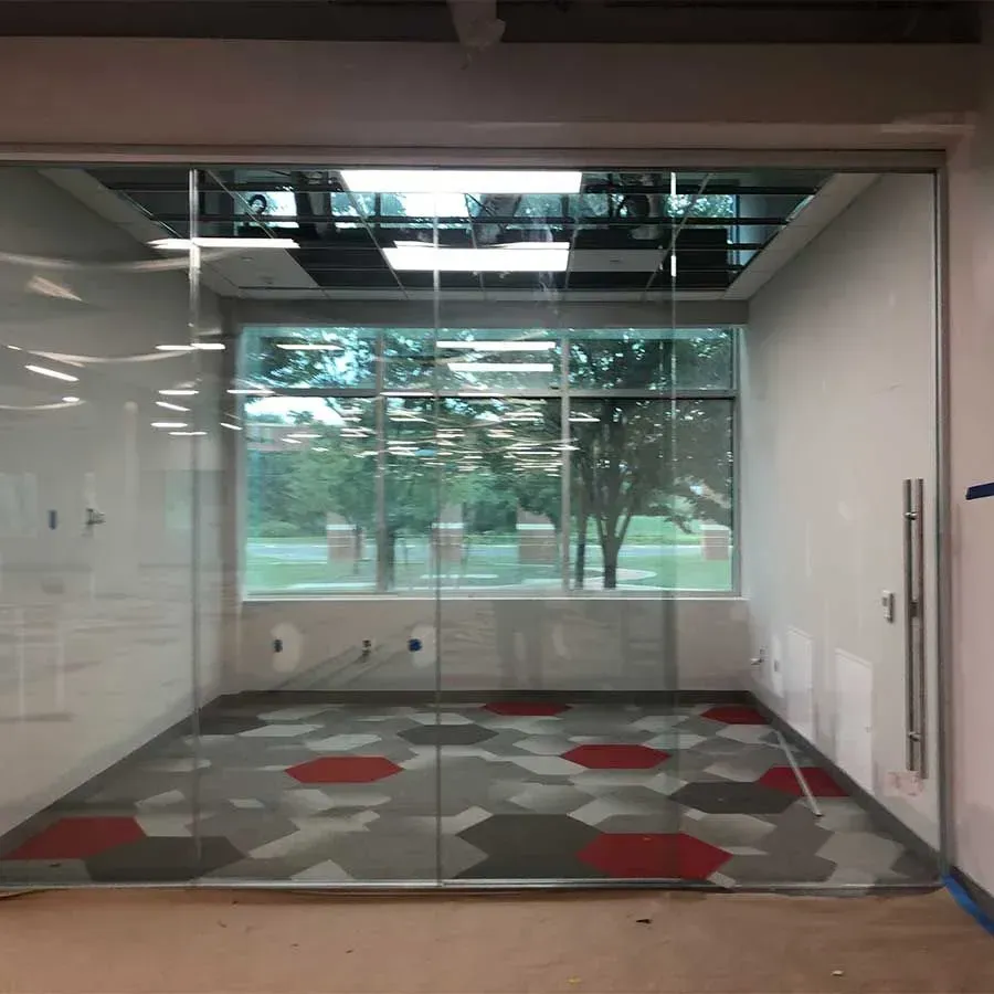 A glass-walled office with a hexagonal patterned floor in shades of grey and red, facing a large window with outdoor views.