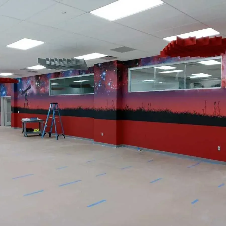 An empty room with a space-themed wall mural, a red lower wall, a ladder, and rolling cart on a light-colored floor.