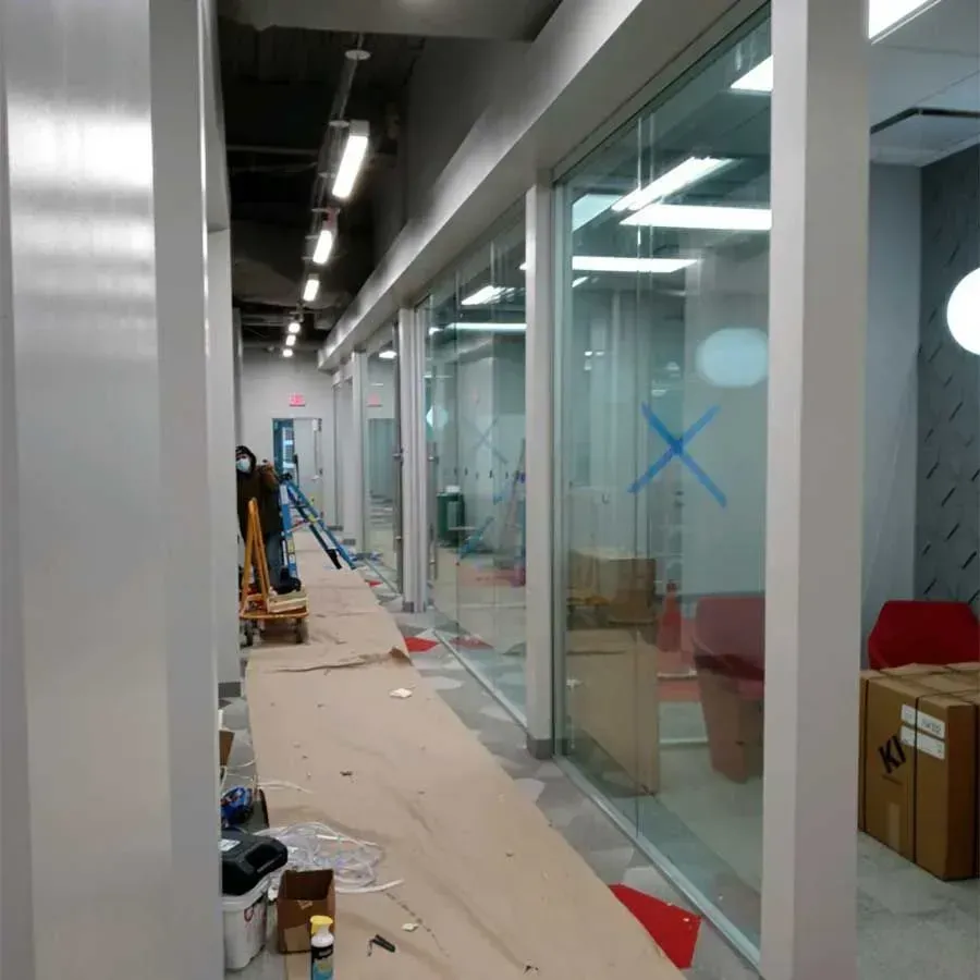 An office hallway under construction with glass partitions, protective paper floor covering, and worker in the distance.