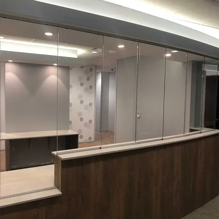 A modern reception desk featuring a wood-panel base, white countertop, and a glass partition separating the service area.